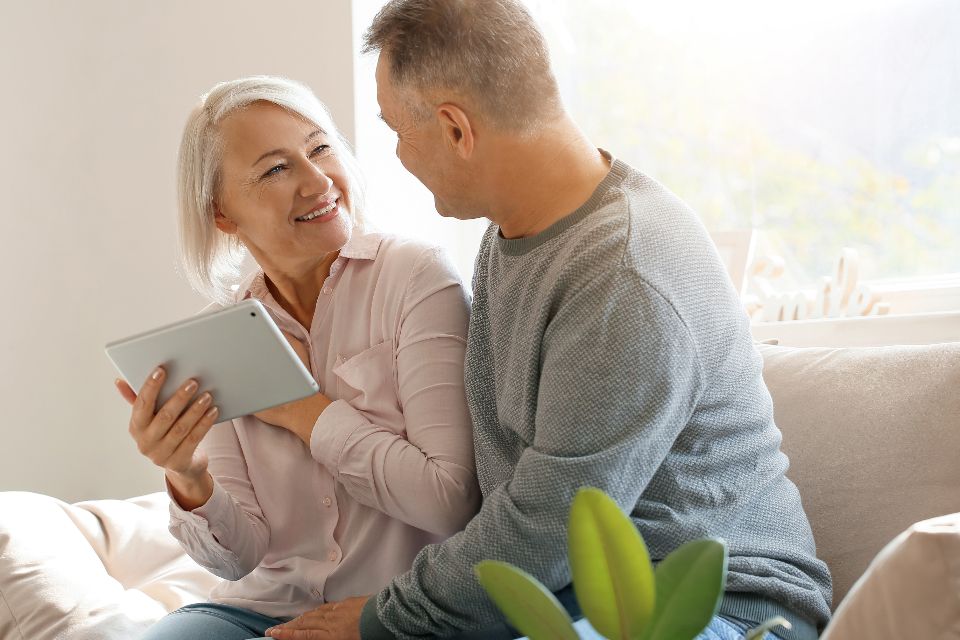 An older couple laughing together on the sofa with a tablet